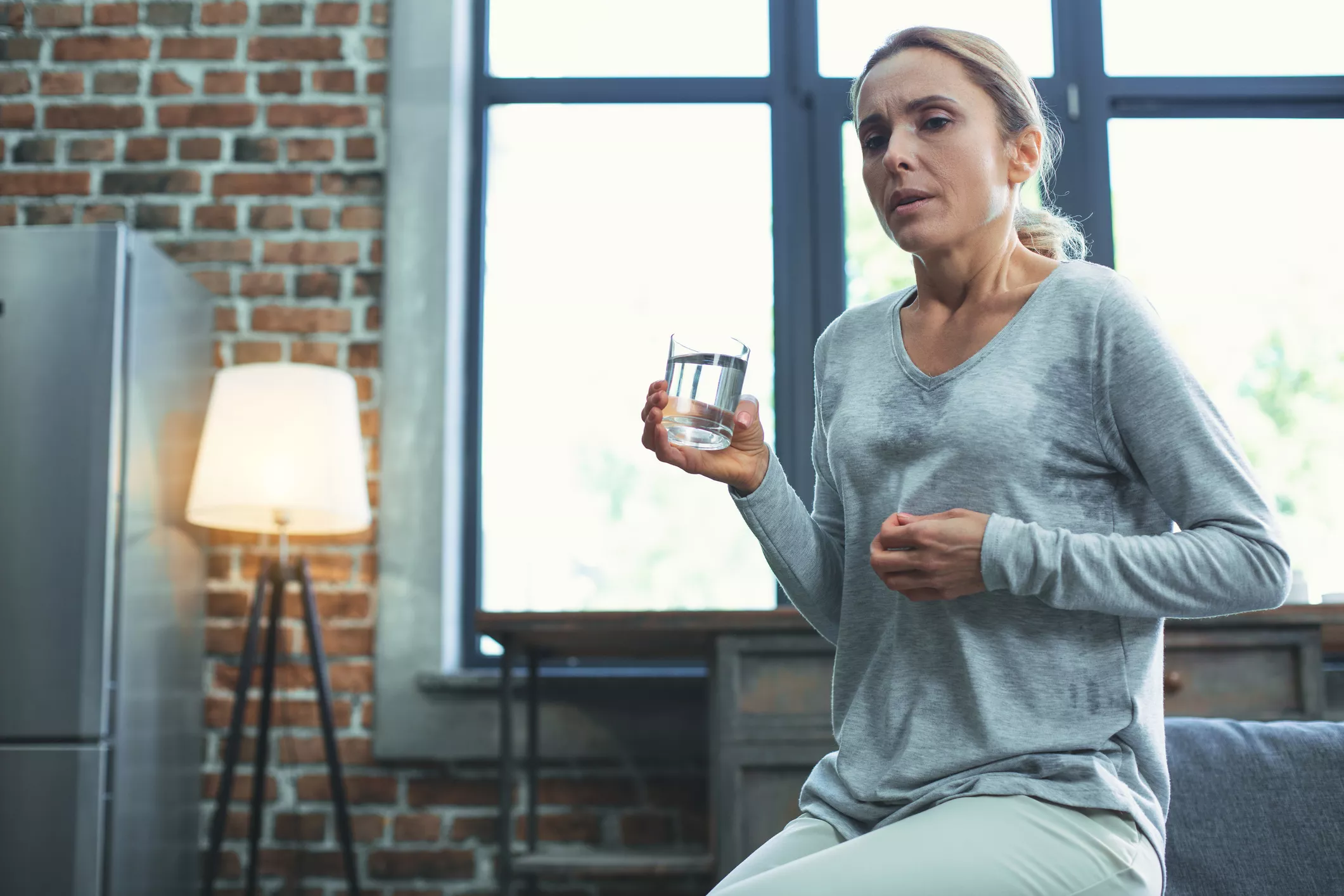 A woman in her living room sweating and holding a glass of water